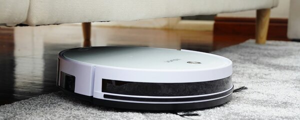 Robot aspirapolvere che pulisce sotto un divano rialzato in una villetta moderna