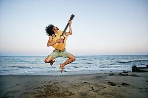 Fotografia artistica Mixed Race man playing guitar and jumping at beach, Peathegee Inc, (40 x 26.7 cm)