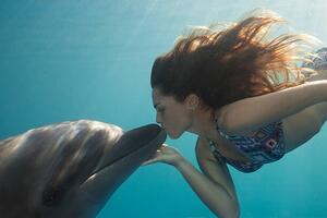 Fotografia Young Woman Kisses Dolphin Underwater Sunbeams, Justin Lewis, (40 x 26.7 cm)