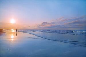 Fotografia Person walking on beach at sunrise, Shannon Fagan, (40 x 26.7 cm)