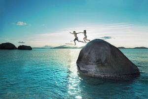 Fotografia artistica Two kids holding hands jumping off rock into sea, Gary John Norman, (40 x 26.7 cm)
