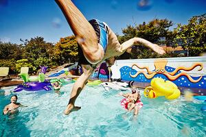 Fotografia Man in mid air jumping into pool during party, Thomas Barwick, (40 x 26.7 cm)