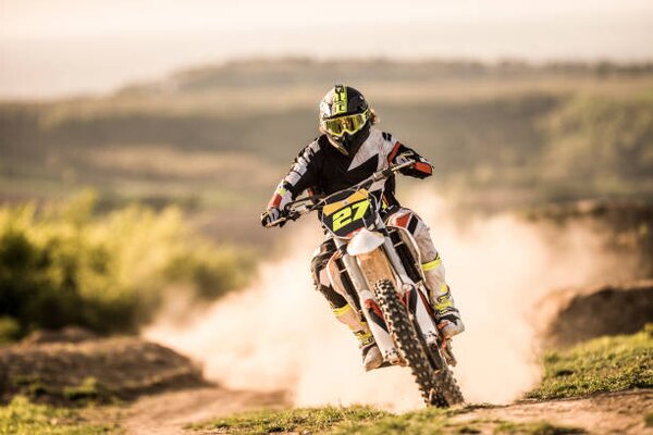 Fotografia Man on dirt bike racing on dirt road in nature, skynesher